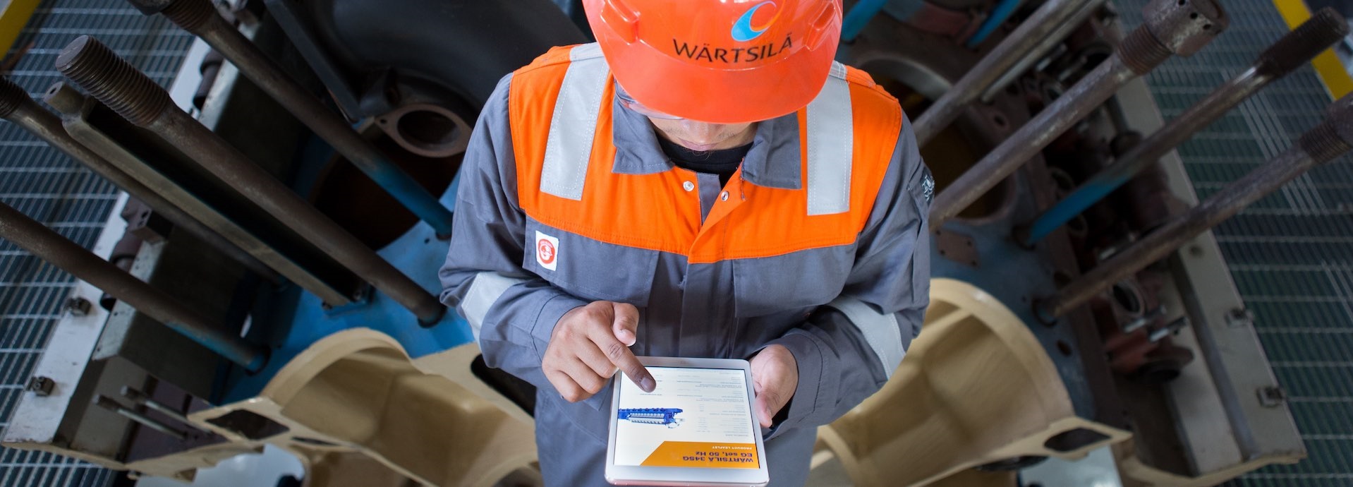 Image of a man wearing Wärtsilä safety gear along with a helmet with the Wärtsilä logo using a tablet