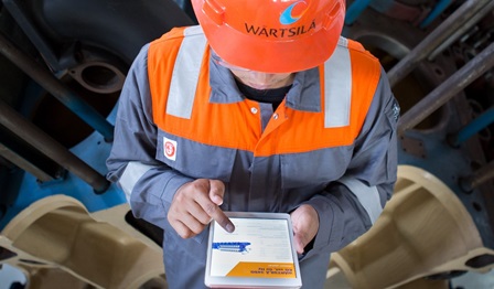 Image of a man wearing Wärtsilä safety gear along with a helmet with the Wärtsilä logo using a tablet