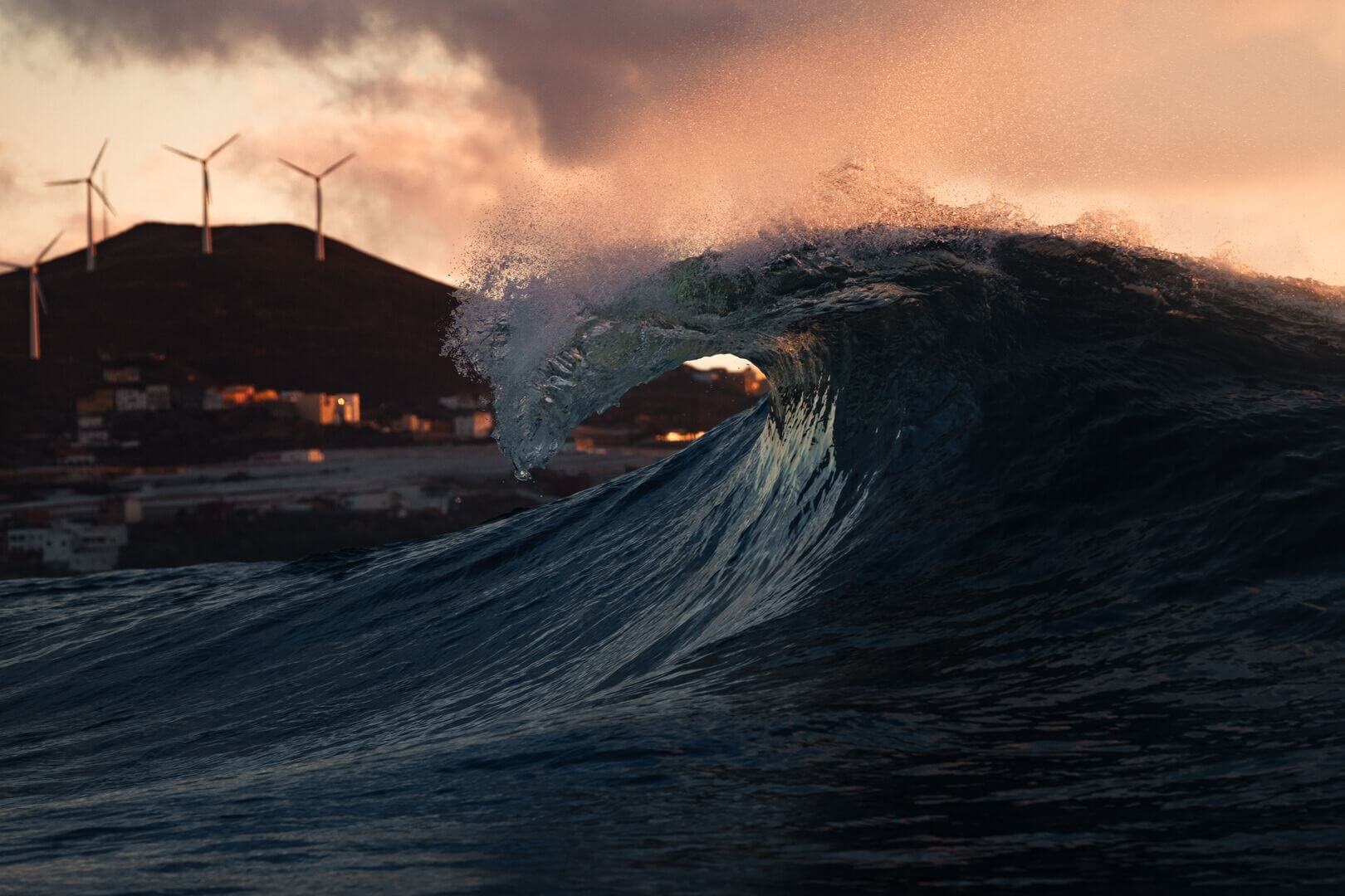 Wave at sea with wind turbines on land in the distance