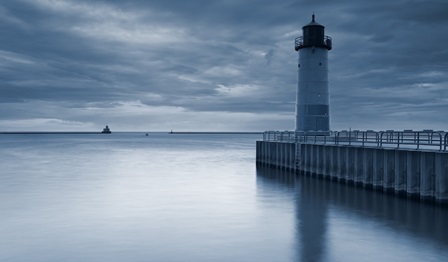 image of a lighthouse next to a pier with ship sailing in the distance