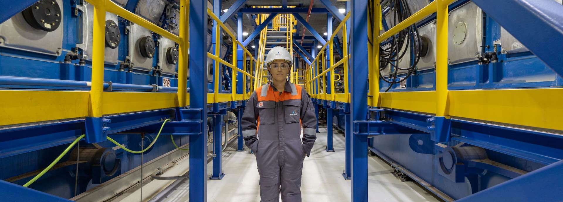 Image of a lady wearing Wärtsilä safety gear standing in the corridor of a power plant with machinery on either side.