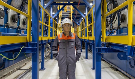 Image of a lady wearing Wärtsilä safety gear standing in the corridor of a power plant with machinery on either side.