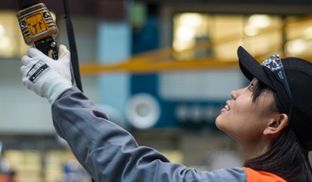 Image of an Asian lady looking up at a piece of machinery she is operating