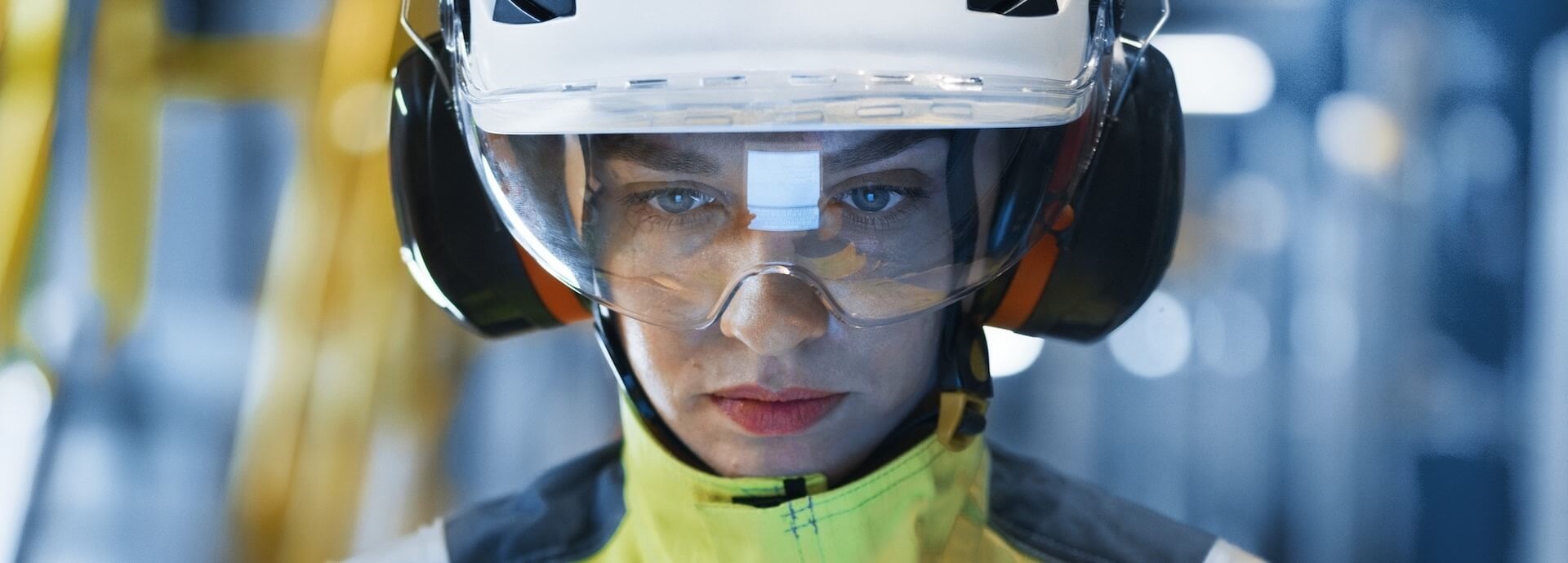 Woman wearing safety headphones and visor. Reflection of tablet on visor.