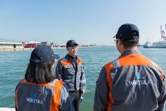 Three Wärtsilian workers standing in a sunny harbour.