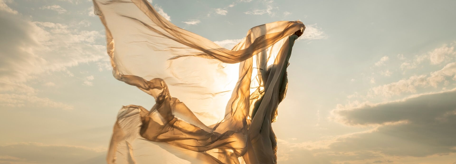 A woman waving a golden transparent fabric in sunshine