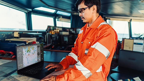 men on a ship bridge using a laptop