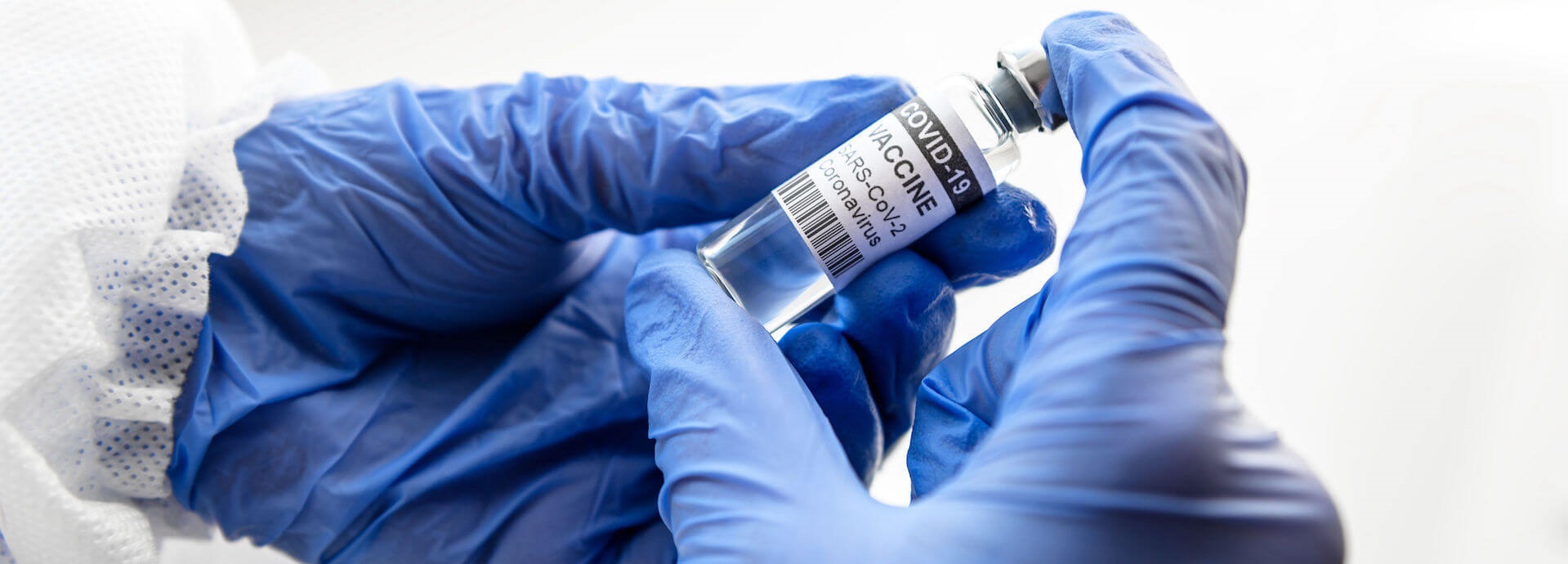 gloved hands holding a vial of vaccine