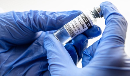 gloved hands holding a vial of vaccine